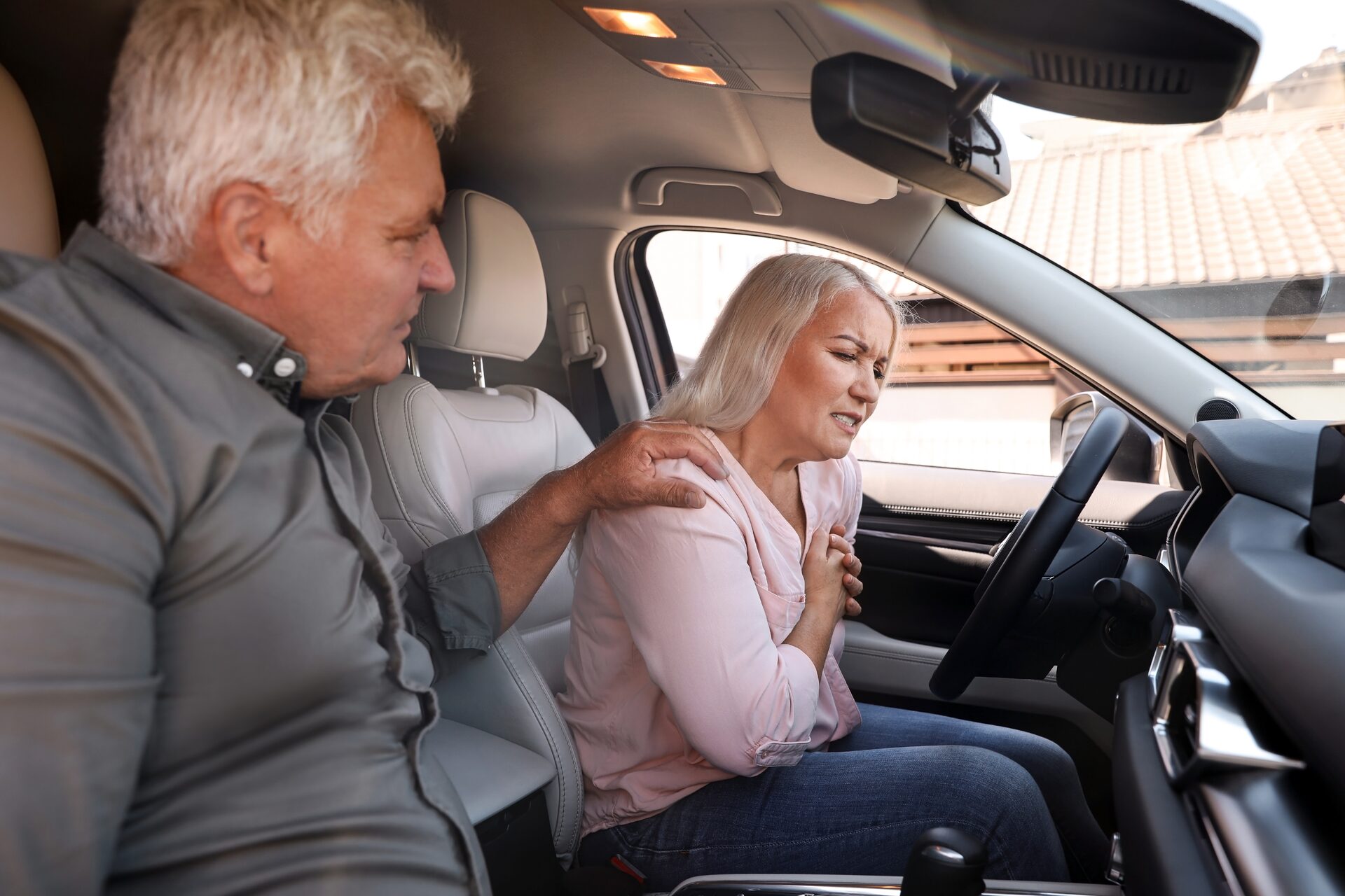 A woman in a car holding her shoulder in pain after an accident while a man helps her