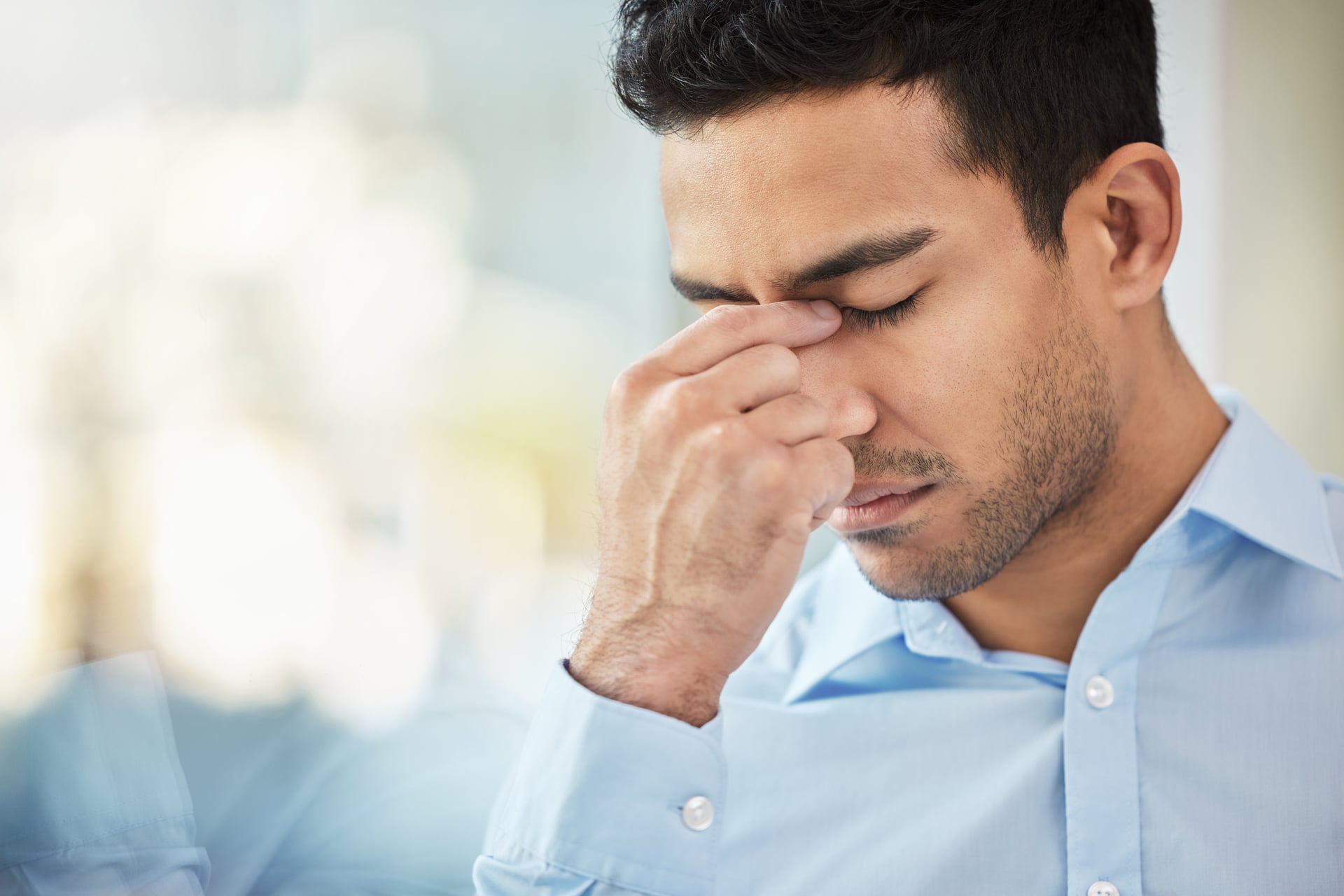 A man pinching the bridge of his nose with his eyes closed, showing sinus pressure and headache pain