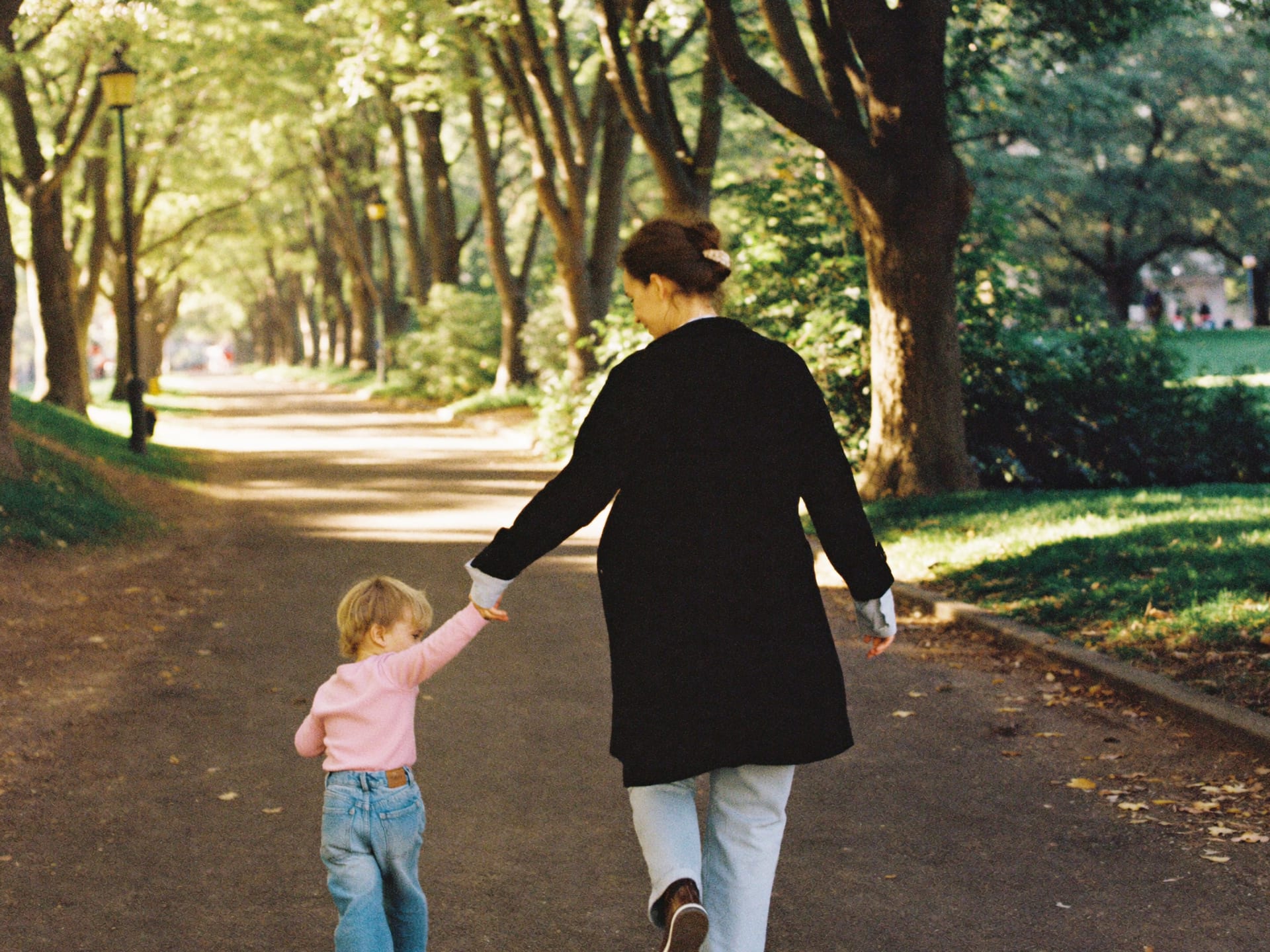 A parent and child walking hand in hand along a sunny park path