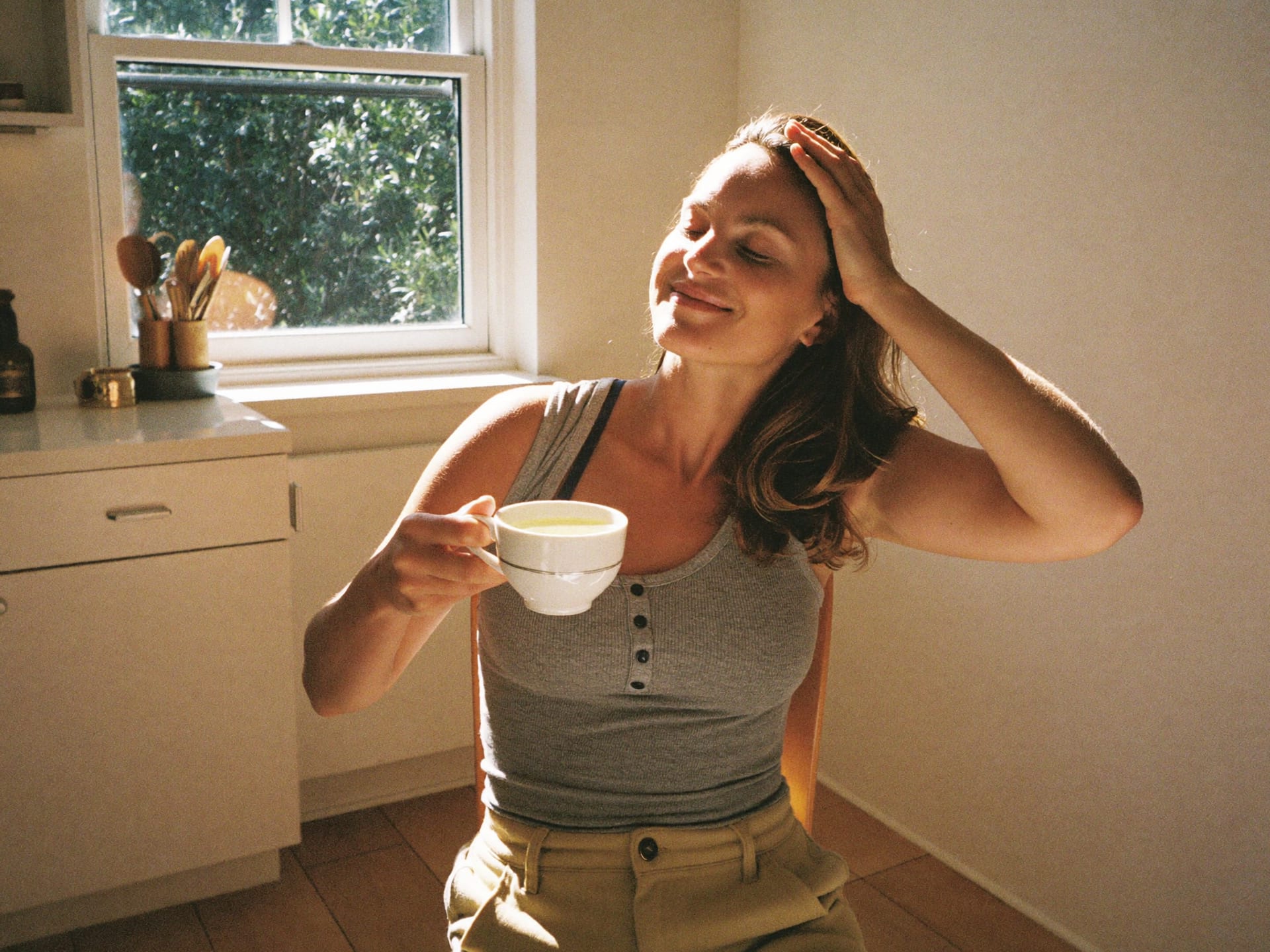A woman relaxing comfortably with tea in a sunny kitchen